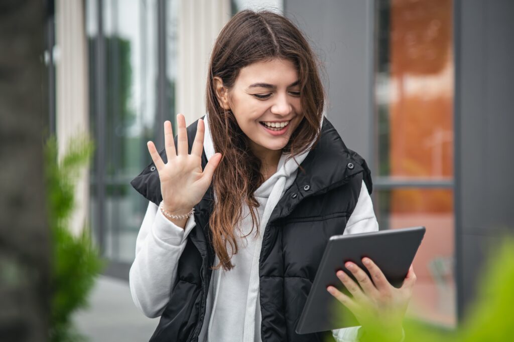 Attractive young woman uses a tablet, communicates by video call outside.